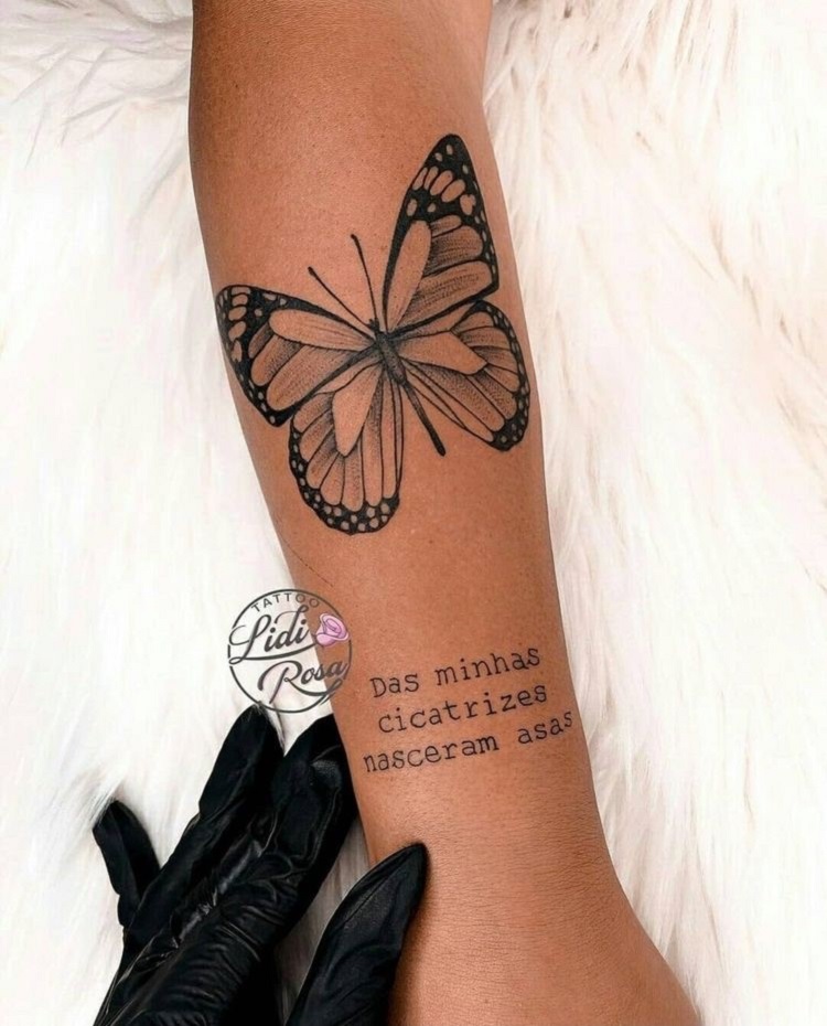 Tatuagem de borboleta com frase "das minhas cicatrizes nasceram asas" em braço