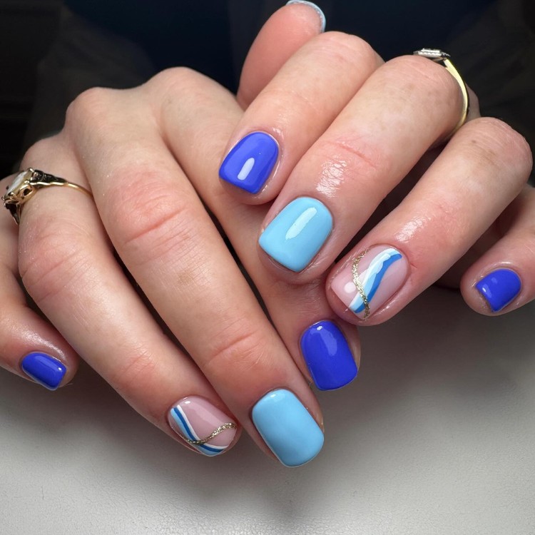 Unhas curtas azuis com anelar bege com detalhes em azul e dourado