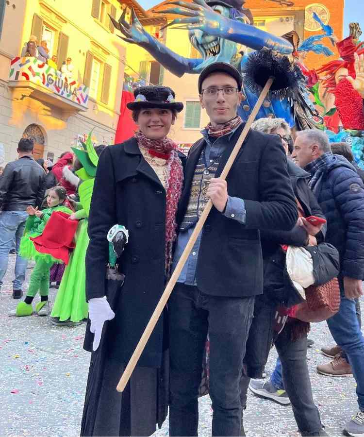 Traje de Dia das Bruxas para namorados: Mary Poppins e Dick Van Dyke. Mary de casaco preto, chapéu, bengala e lenço. Ele de terno preto, camisa azul, colete colorido e boina 