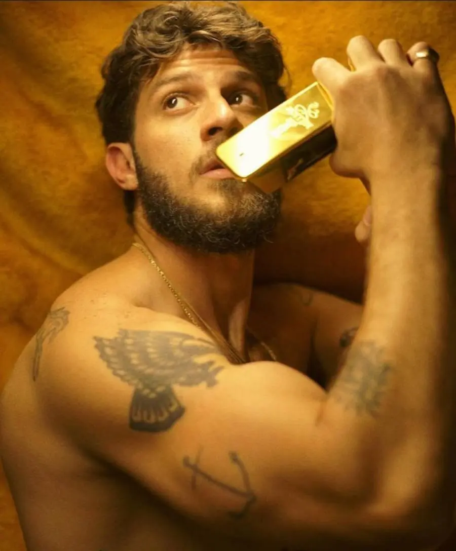 Foto de Chay Suede com vidro de perfume na boca e foco na tatuagem de âncora