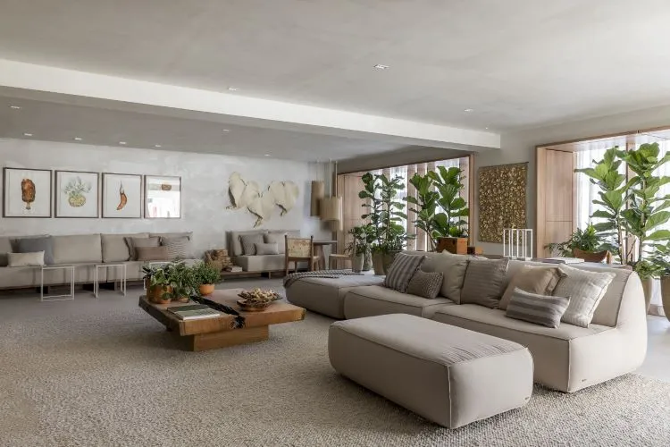 Decoração de sala de estar que contribui com a saúde mental, com cores neutras, sofás e poltronas beges, plantas na decoração, itens decorativos de folhas e quadros em tons terrosos