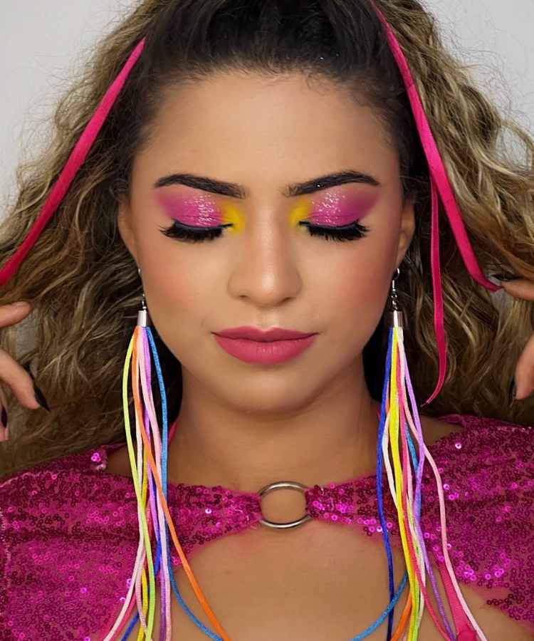 Mulher de pele clara usando sombra rosa e amarela com glitter e batom rosa 