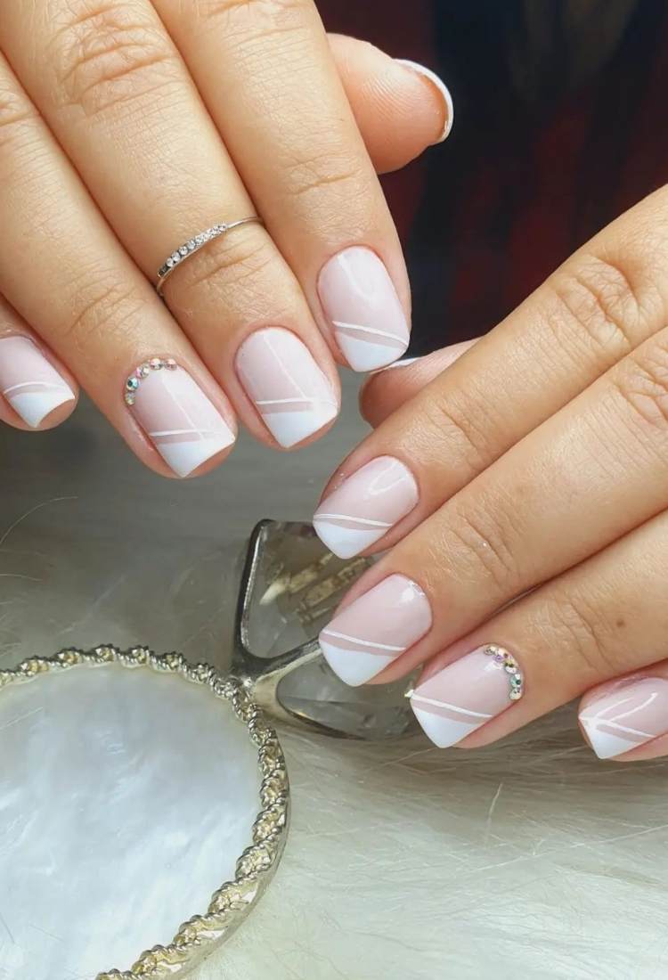 Unhas quadradas curtas com branco na diagonal e pedrarias 