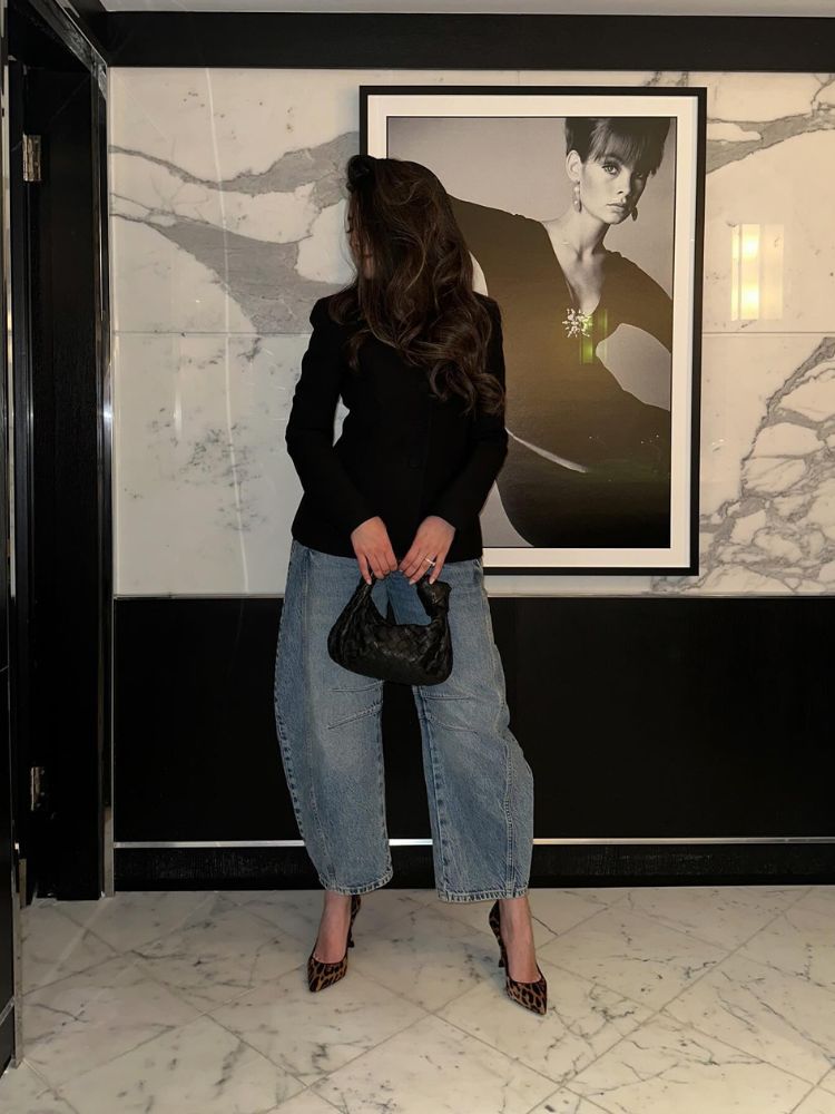 Mulher de pele clara de blazer preto, calça jeans barrel e salto