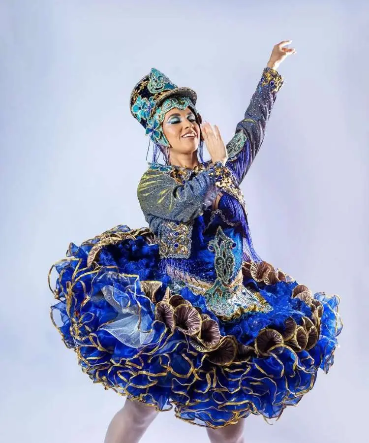 Imagem de uma rainha da quadrilha em festa junina, usando um vestido azul vibrante com babados e detalhes dourados. Ela sorri e posa elegantemente com um chapéu ornamentado, representando a beleza e a tradição das festividades juninas. Fontes