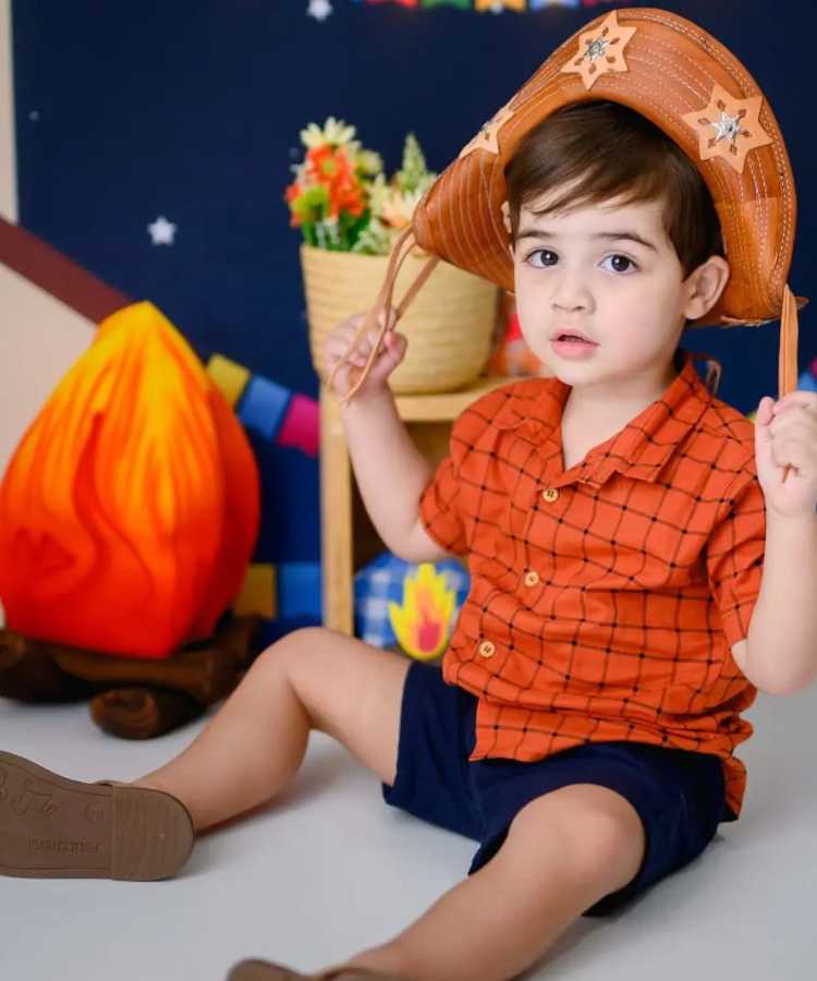 Menino com camisa xadrez vermelha e chapéu de cangaceiro, look de festa junina