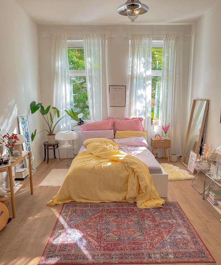 Quarto de casal com espelho retangular apoiado na parede. Cores predominantes: amarelo, rosa, branco, vermelho, azul