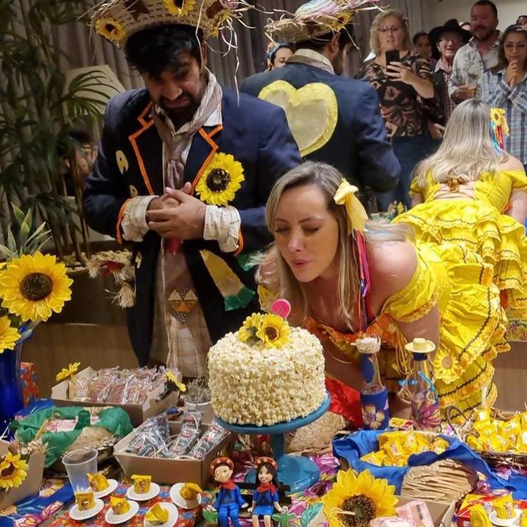 Noiva caipira assoprando vela de volo de pipoca de festa junina ao lado do seu noivo
