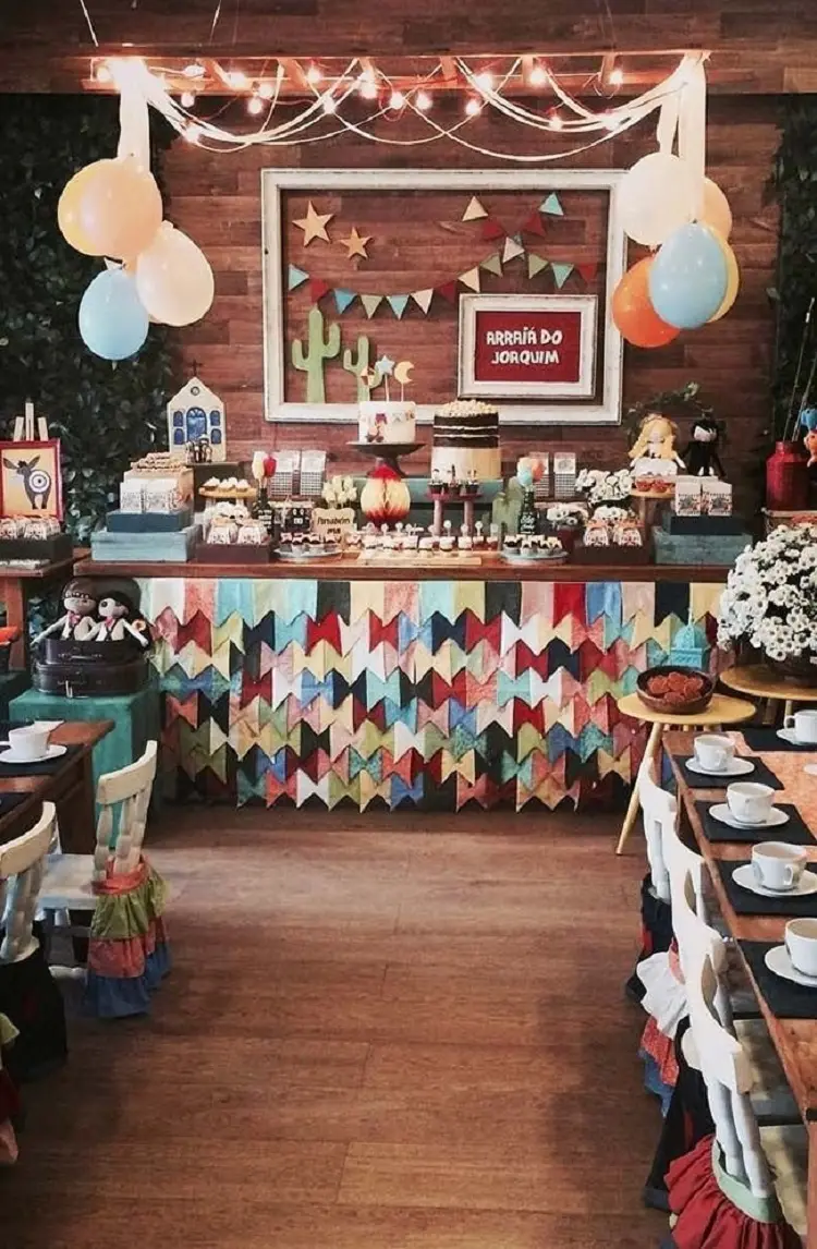 A imagem representa decoração para festa junina. Contém doces e comidas típicas, chapéus de palha, quadros, babado de bandeirinhas