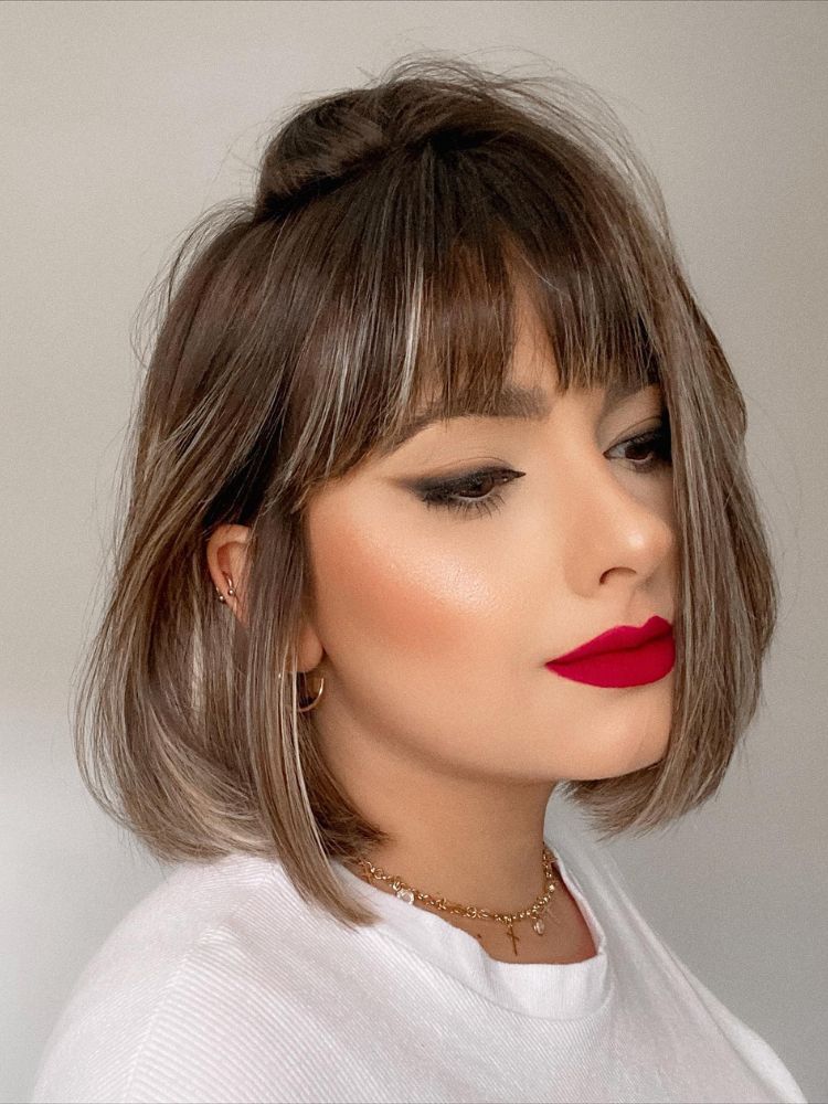 Mulher de pele clara usando blusa branca e cabelo chanel com franja reta