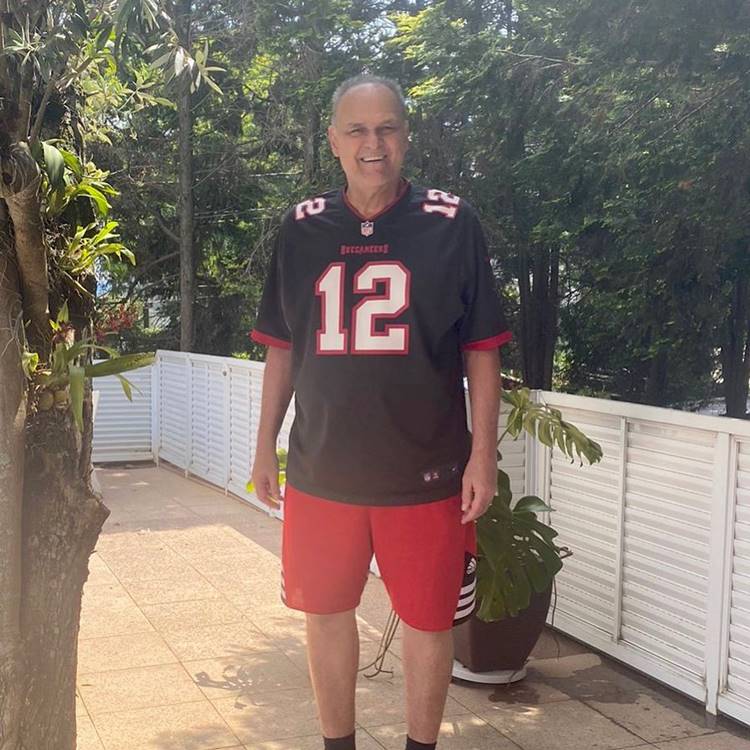 O ex-jogador de basquete hoje em dia, em foto de pé em área externa de casa com plantas e árvores