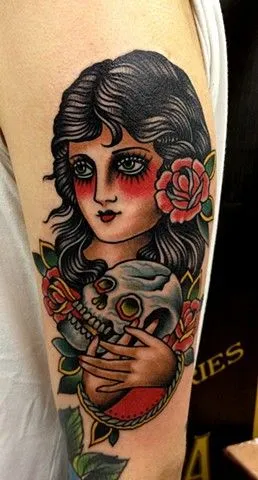 Tatuagem Old School de cigana com cabelo preto, flor vermelha, e segurando uma caveira branca