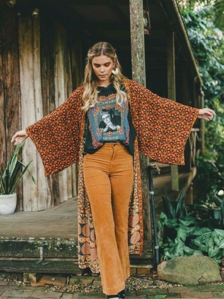 Mulher de pele clara usando blusa preta, kimono bordado e calça bege