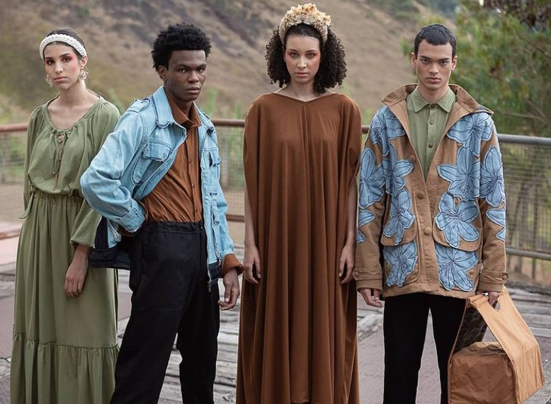 Quatro modelos posando lado a lado ao ar livre com peças da coleção Conspiração de Ronaldo Silvestre, com jaquetas jeans e vestidos soltos e longos em verde e marrom