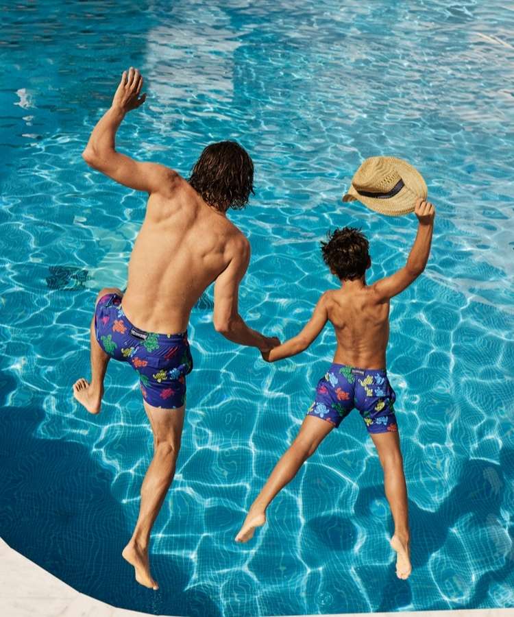 Foto de pai e filho pulando na piscina usando calções combinando da Vilebrequin