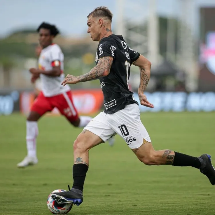 Roger Guedes conduzindo a bola próximo a um jogador do RB Bragantino que está desfocado, assim como o fundo, na foto.