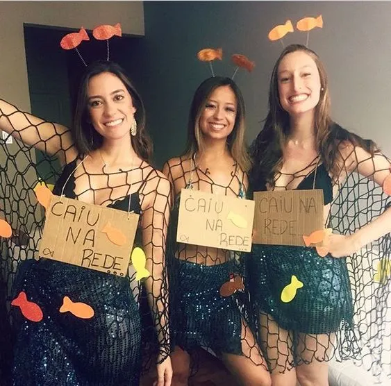 3 mulheres com look preto com rede de peixes e placa "caiu na rede..."