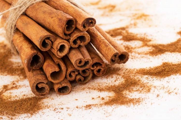 foto de paus de canela empilhados em superfície branca com canela em pó canela em pau