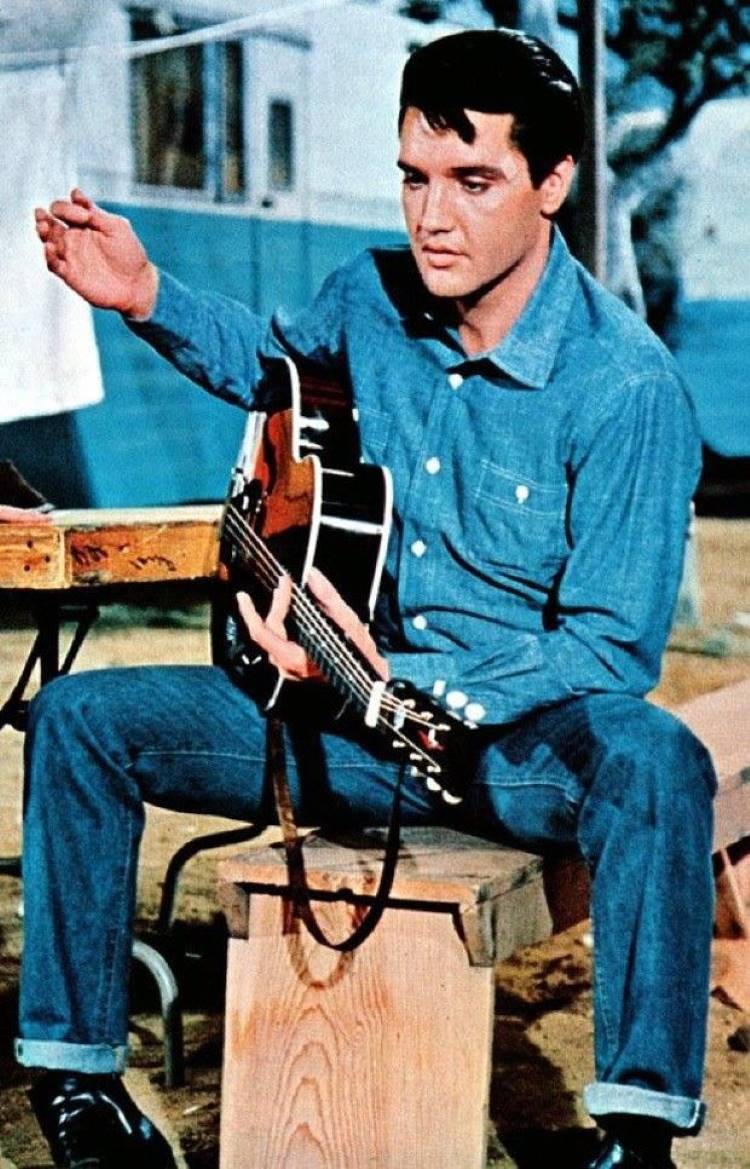 Elvis Presley usando look all jeans sentado com violão