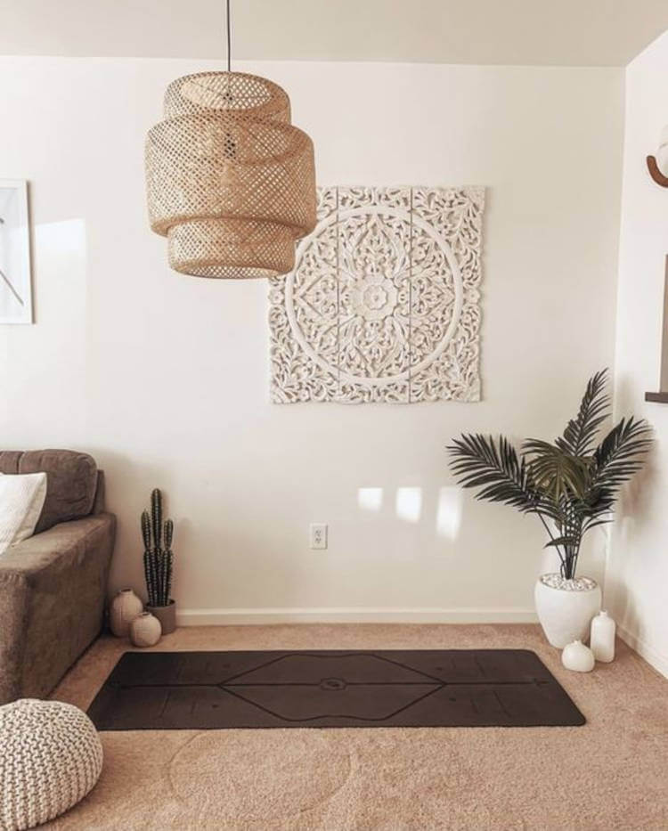 Cantinho zen na sala, com carpete, sofá marrom, vasos de planta e quadro branco na parede