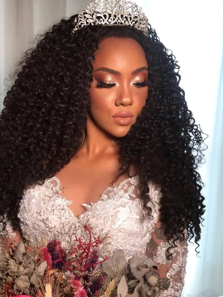 Mulher de pele negra com vestido de noiva, cabelo solto, segurando buquê de flores rosas e usando maquiagem iluminada, com batom nude e cílios chamativos