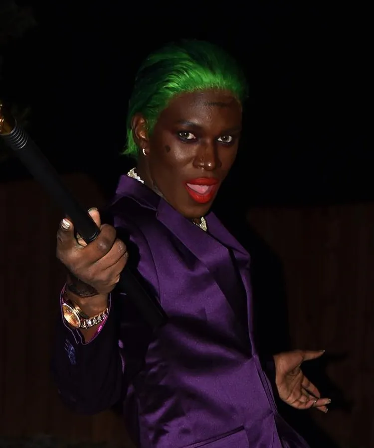 Homem de pele negra maquiado de coringa para o Halloween, usando cabelo verde e terno roxo 