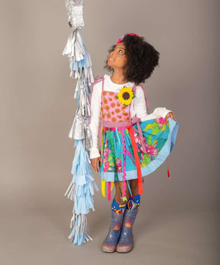Menina com vestido de festa junina, com blusa branca por baixo e bota de glitter