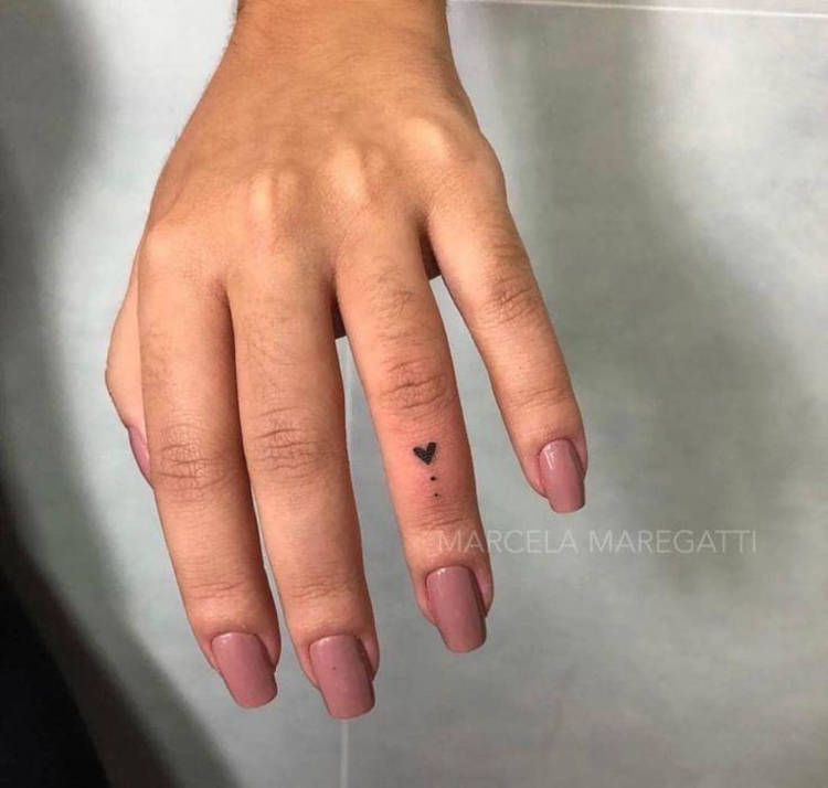Mão de pele clara com esmalte nude e tatuagem de coração no anelar