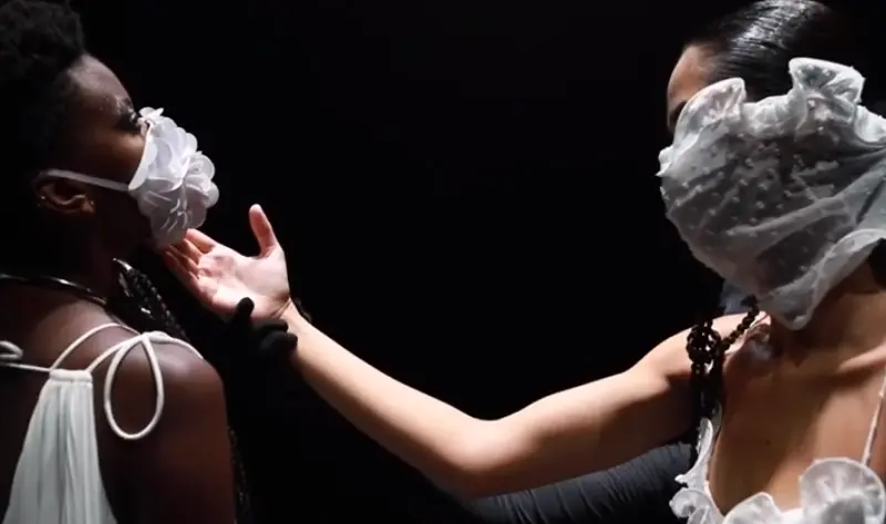 SPFW: Duas modelos se olhando. A da esquerda usa máscara branca com bordado e da direita usa máscara transparente com flocado. 