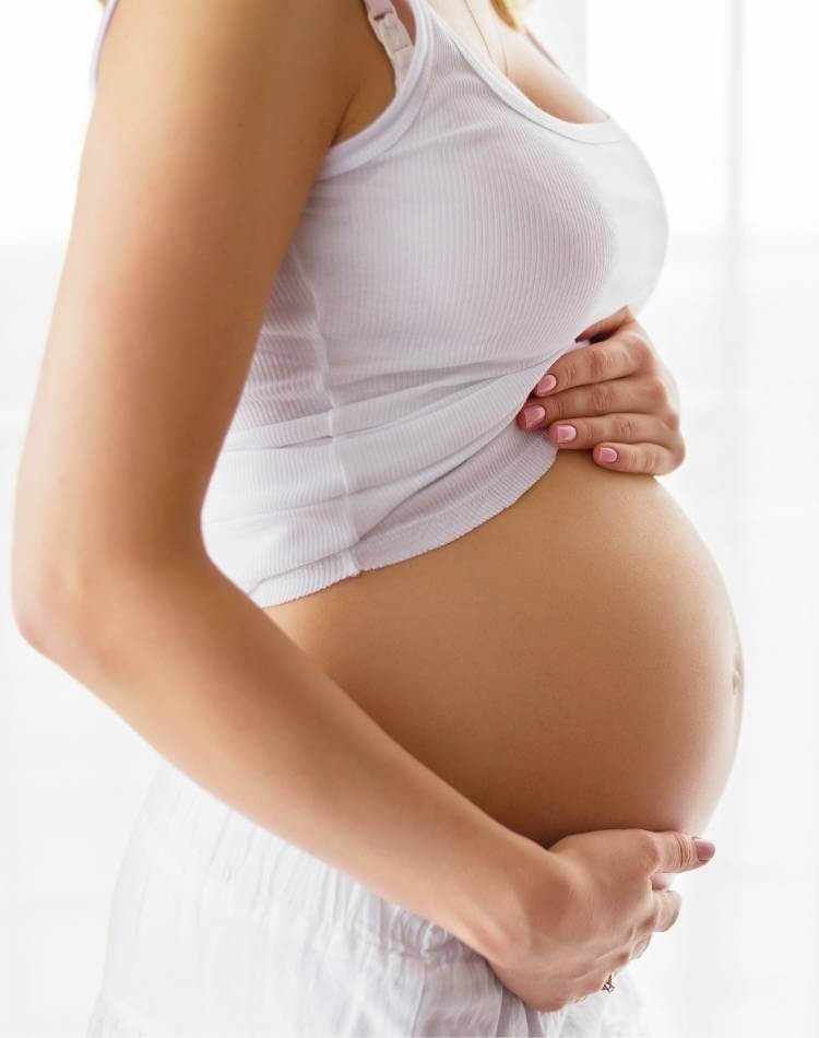 Mulher grávida com regata levantada expondo a barriga.