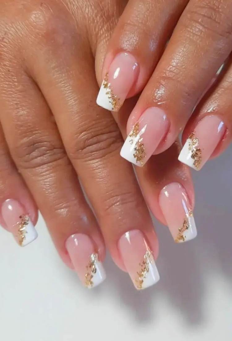 Unhas quadradas médias com fundo nude e detalhes brancos diagonais com folha de ouro