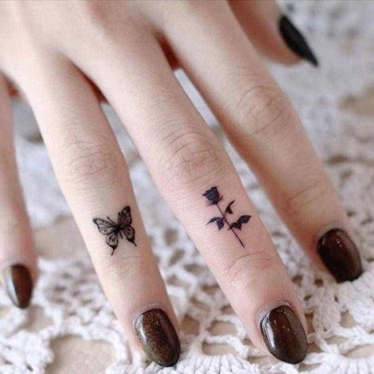 Mão com esmalte marrom, borboleta no anelar e rosa no médio 