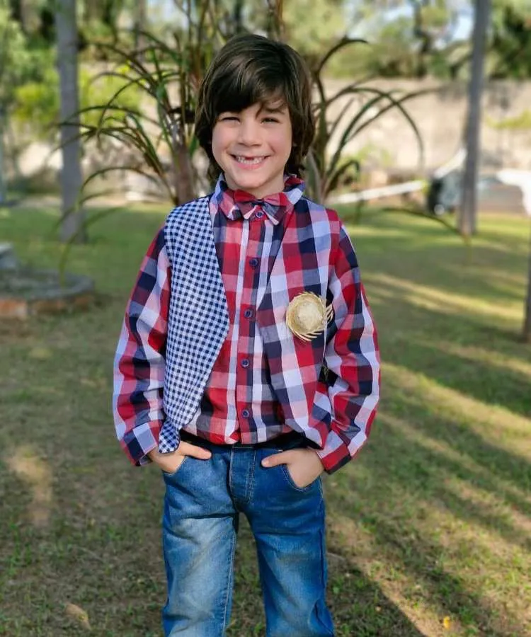Menino usando camisa xadrez vermelha, colete e calça jeans.
