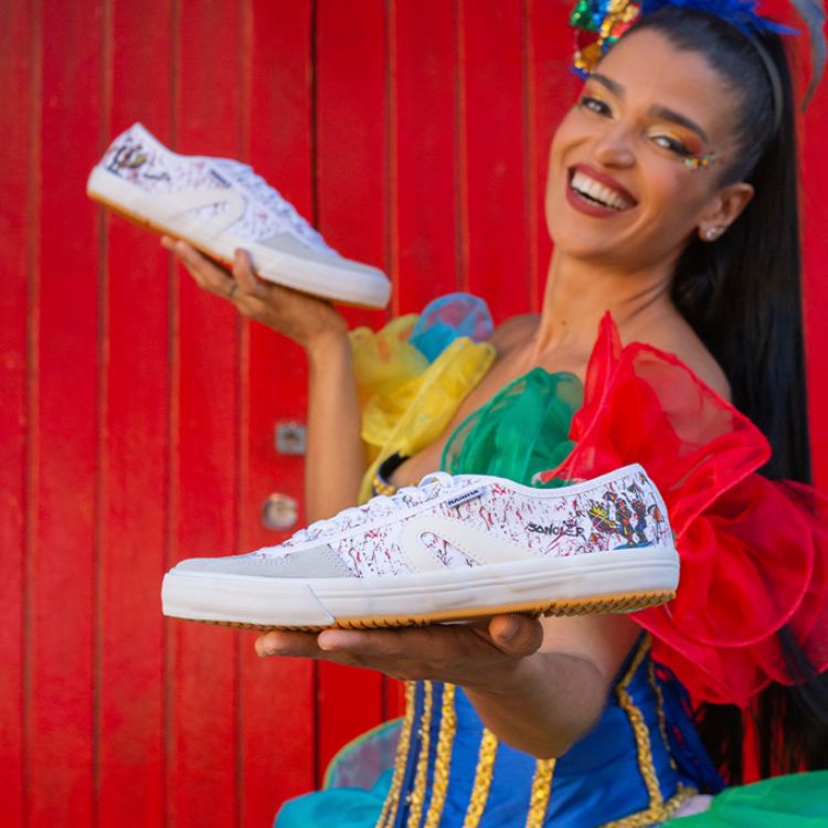 Mulher de pele morena com roupa colorida segurando tênis VL 2500 Frevo