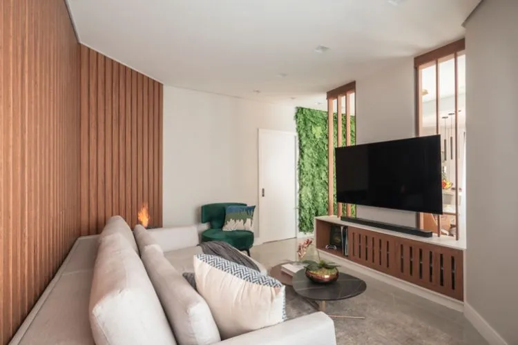 Sala com parede de madeira, branca e com jardim vertical, sofá claro, mesa de centro escura e poltrona verde musgo