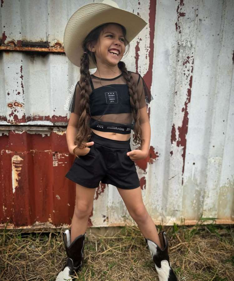 Menina usando look country preto com chapéu e bota western.

