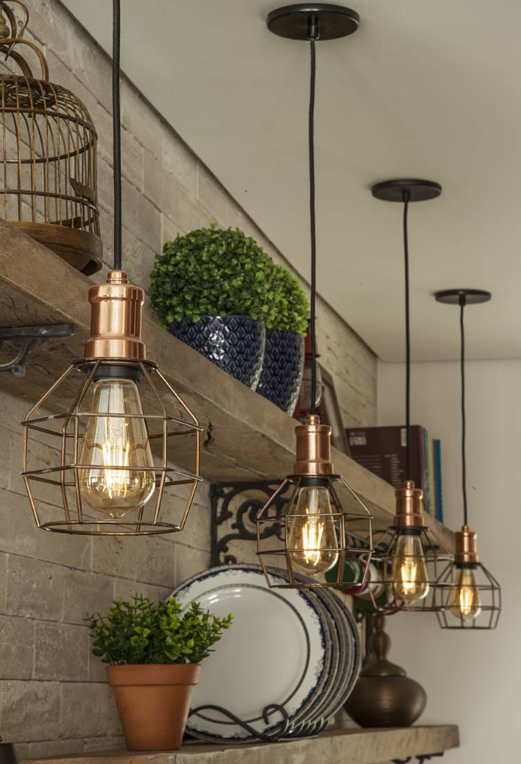 Vista próxima de prateleiras de madeira em uma cozinha rústica moderna. Destaque para as luminárias pendentes em tom cobre com design industrial, iluminando pratos decorativos e pequenos vasos de plantas.







