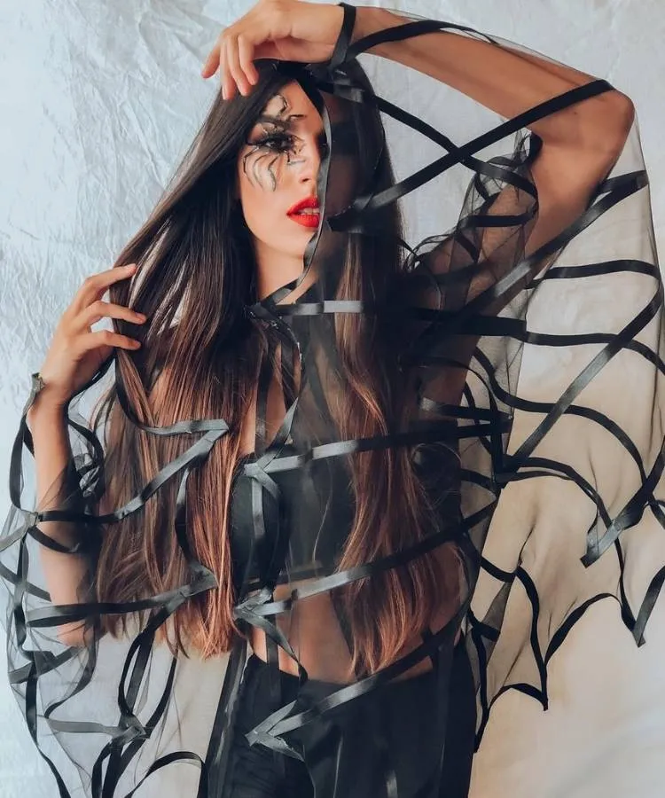 Foto de mulher morena usando capa de teia de aranha e delineado de Halloween