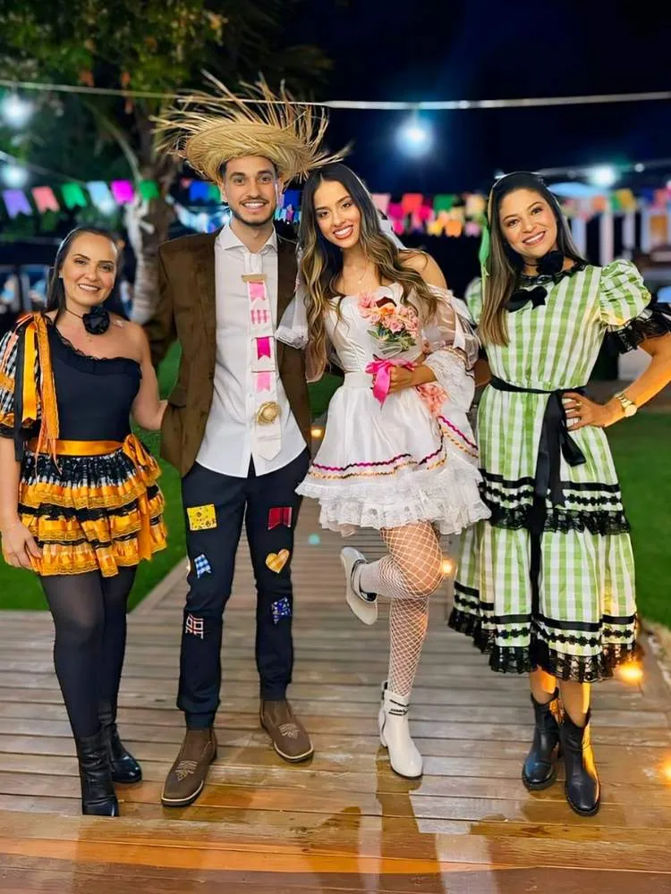 4 pessoas, sendo 3 mulheres e 1 homem, com trajes juninos, sendo uma mulher de novinha