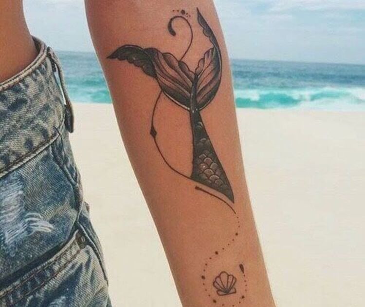 Tatuagem feminina de uma cauda de sereia e uma concha no braço