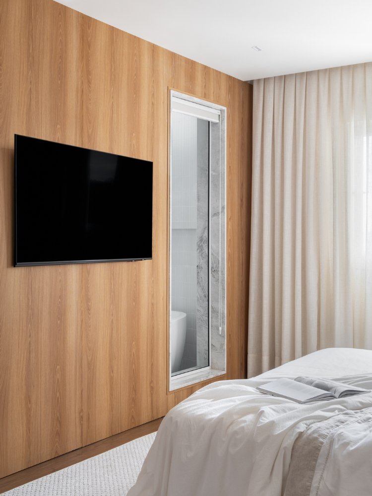 Suíte com parede de madeira com TV e porta de vidro para o banheiro 