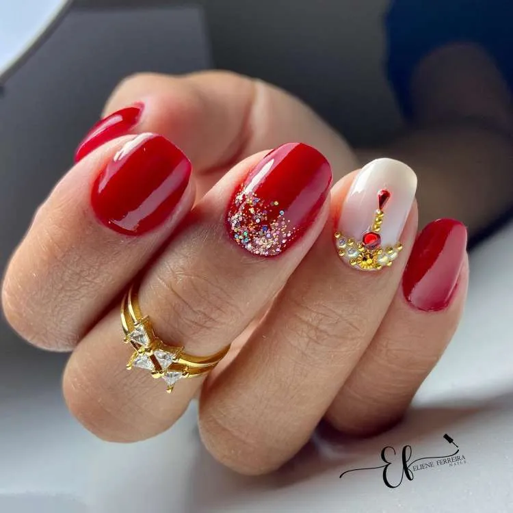 Unhas vermelhas decoradas, glitter prata no dedo do meio e pedraria vermelha na filha única de cor branca