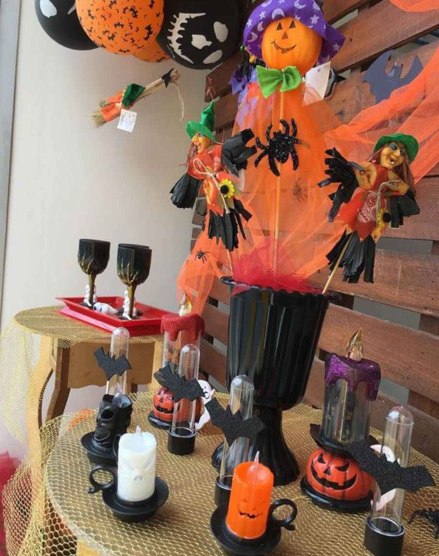 Imagem de decoração de Haloween com enfeites como bola de caveira e morcegos, vela de halloween, bruxinha, aranhas e copos com dedos de caveira