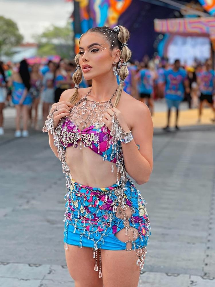 Mulher de pele clara com top e saia de abadá azul e roxo, além de acessório de corrente com gotas 