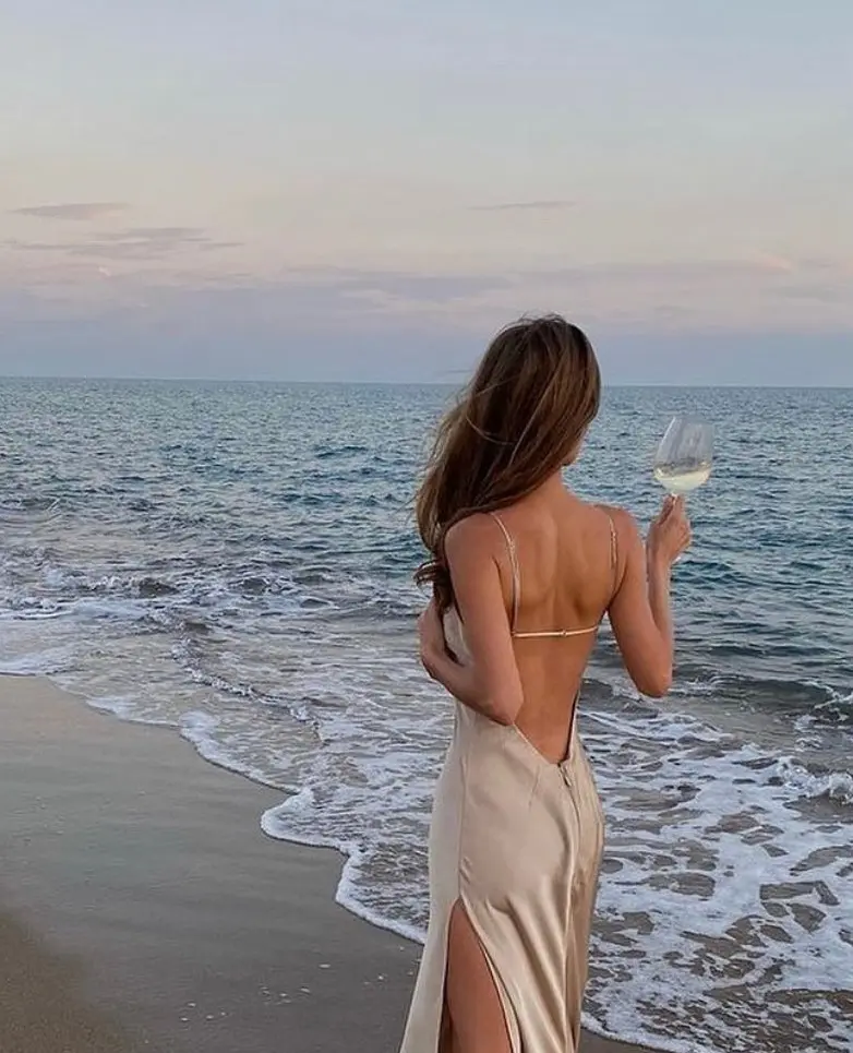 Frase para foto pensativa mulher na praia com vestido bege tomando champagne