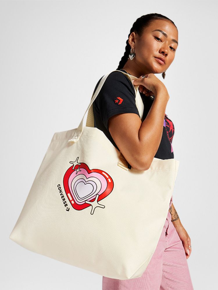 Foto de mulher usando camiseta preta, calça rosa e ecobag da Converse com coração
