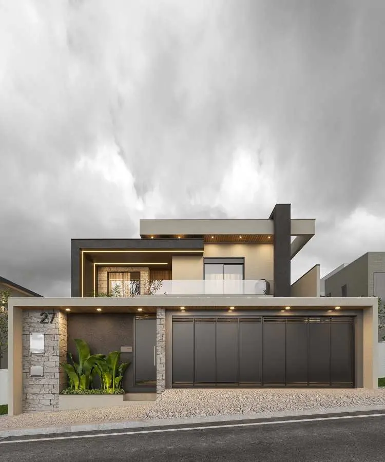 Fachada de casa contemporânea de dois andares com design sofisticado. Garagem com portão preto metálico, parede de pedra com número "27" destacado, e jardim decorativo com plantas verdes à esquerda. Varanda com guarda-corpo de vidro, iluminação embutida e detalhes elegantes em concreto e madeira. O céu nublado contrasta com o tom neutro da construção, emoldurando o projeto arquitetônico.