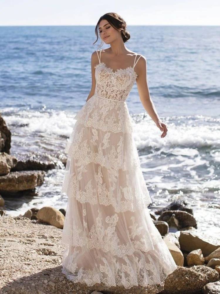 Mulher de pele clara em pedras com mar ao fundo usando vestido de alça com rendas e babados