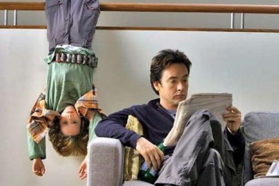 Foto dos atores John Cusack (David Gordon) e Bobby Coleman (Dennis) de "Ensinando a Viver". Davis está sentado em sofá e lendo jornal, enquanto Dennis pendurado pelos pés num local de madeira.