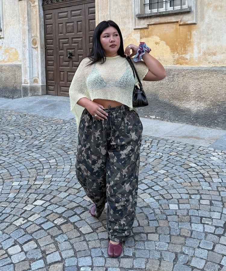Mulher usando blusa branca assimétrica e calça com estampa camuflada